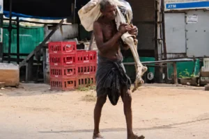 Elderly man in Odisha carrying skeletal remains wrapped in cloth near a bank during a protest over withdrawal of deceased sister’s money.