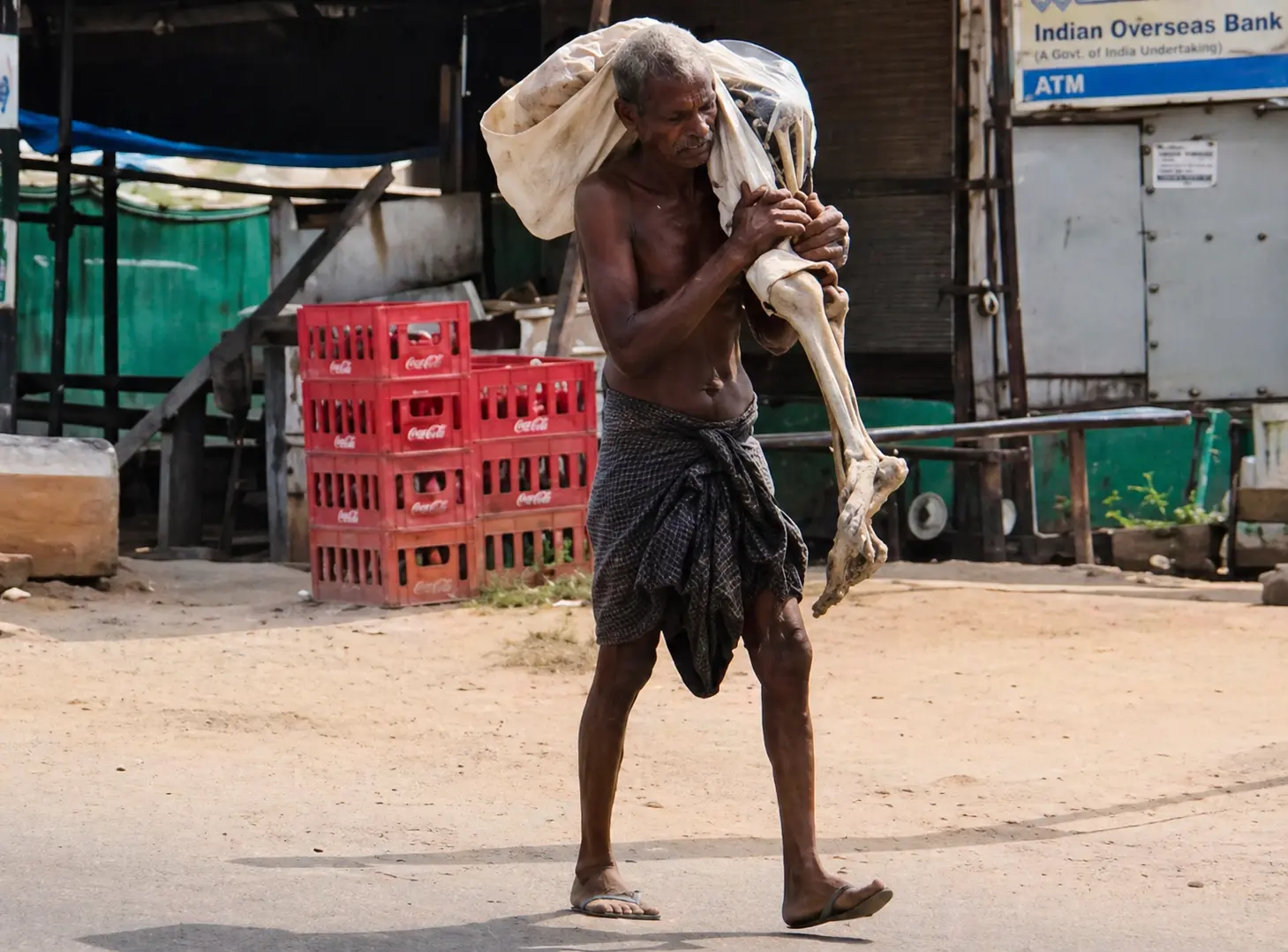 Elderly man in Odisha carrying skeletal remains wrapped in cloth near a bank during a protest over withdrawal of deceased sister’s money.